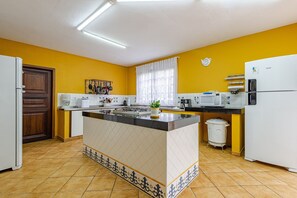 A kitchen with a central island, white appliances, and yellow walls. - Fazenda Realeza (Pedra Bela)