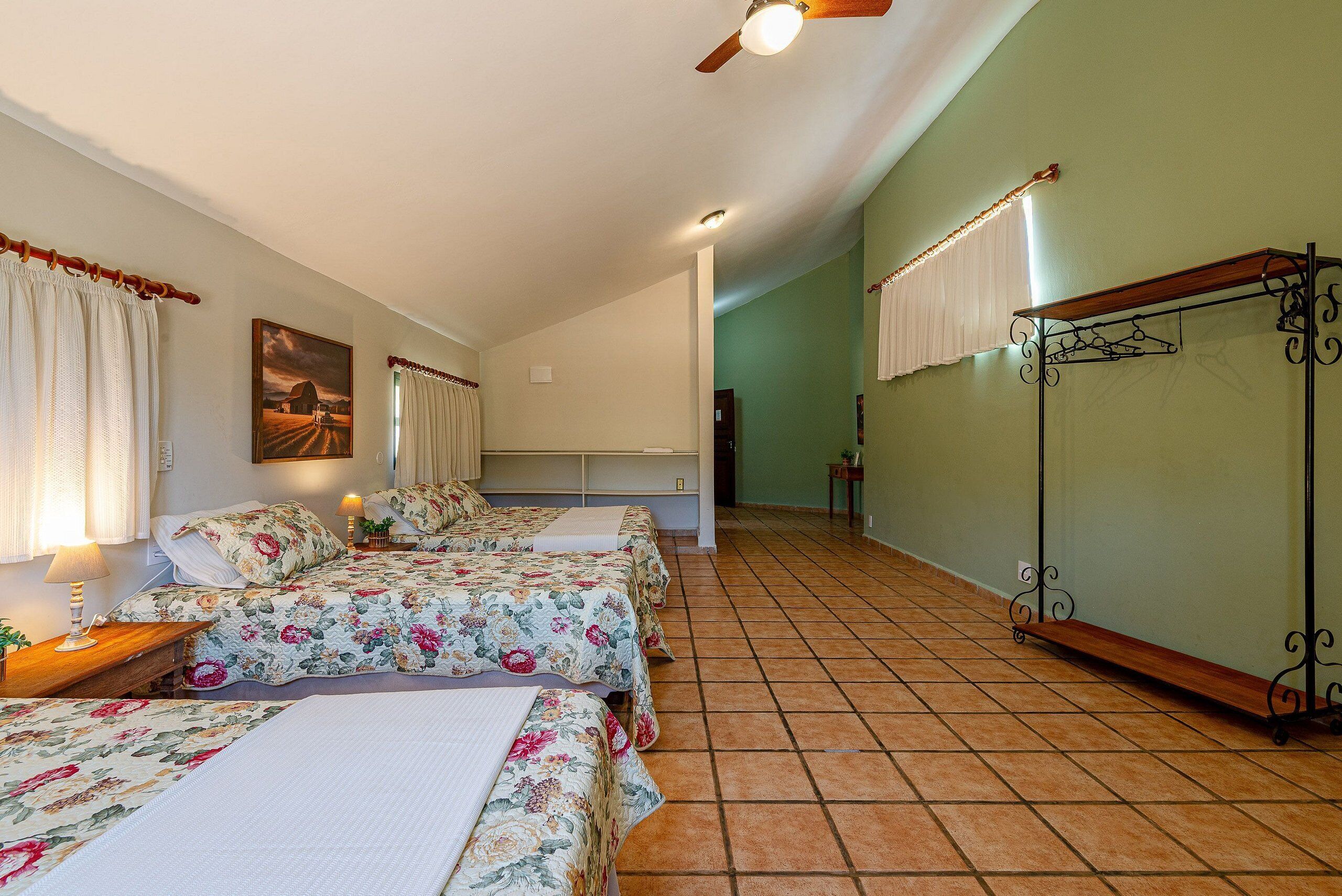Une chambre d’hôtel avec deux lits, un ventilateur de plafond, un tableau au mur et un sol carrelé.