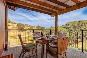 A covered outdoor dining area with a table set for two, surrounded by wicker chairs with cushions. - Fazenda Realeza (Pedra Bela)