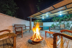 An outdoor patio with a fire pit, wooden benches, and a pool area. - Fazenda Realeza (Pedra Bela)