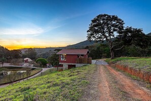 A red house with a stone foundation, a dirt path, and a pond. - Fazenda Realeza (Pedra Bela)