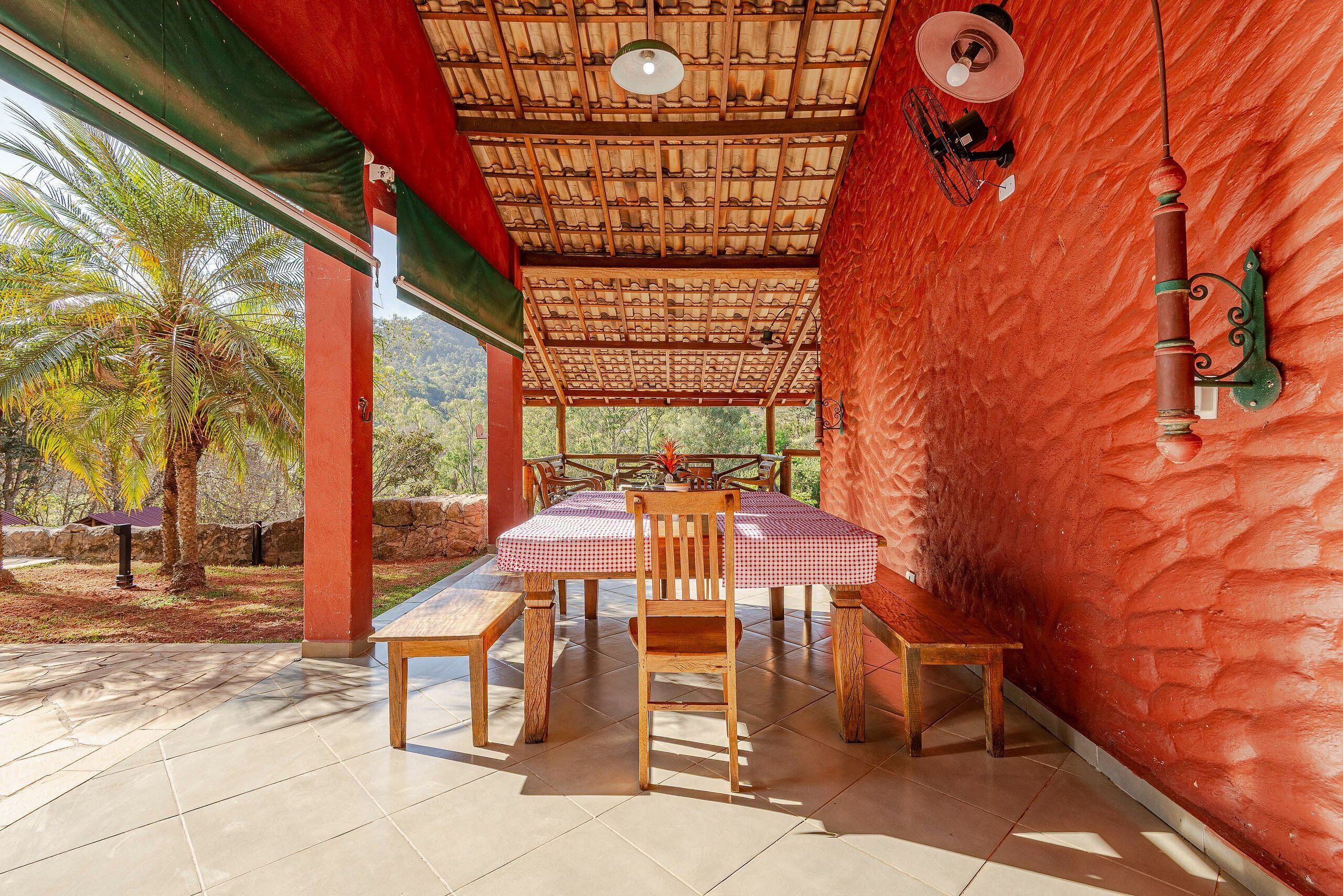 An outdoor patio with a table and chairs, a red wall, and a thatched roof.