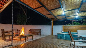 Un patio al aire libre con piso de madera, un brasero, asientos y una piscina.