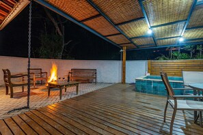 An outdoor patio area with wooden flooring, a fire pit, seating, and a pool. - Fazenda Realeza (Pedra Bela)