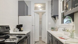 Una cocina compacta con armarios blancos, una estufa negra y un ventanal sobre el fregadero.