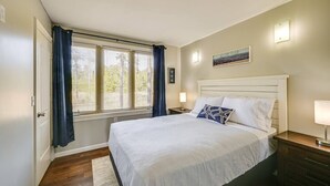 Une chambre à coucher comprenant un lit, des tables de chevet, une fenêtre avec des rideaux, un luminaire fixé au mur et un tableau encadré.