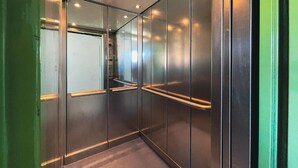 Un ascenseur moderne aux parois métalliques et aux portes en verre, doté d’une main courante et d’un éclairage encastré.