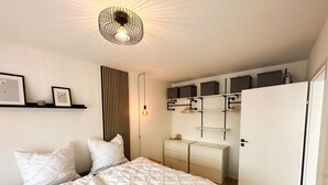 Une chambre à coucher comprenant un lit, des tables de chevet, une armoire et un luminaire suspendu.