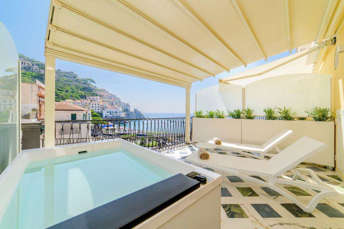 A rooftop terrace with a hot tub, lounge chairs, and a view of the coastline.