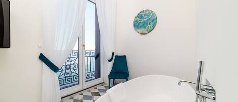 Un baño con una bañera independiente, ducha, una silla azul y un plato decorativo en la pared.