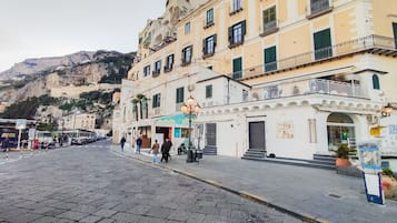 A cobblestone street with buildings, a mountain in the background, and a few people walking.