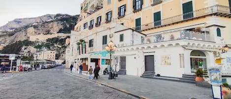 A cobblestone street with buildings, a mountain in the background, and a few people walking.