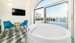 Un baño moderno con una bañera grande, dos sillas azules, una mesita pequeña y un televisor montado en la pared.