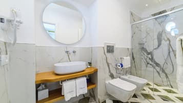 Ein modernes Badezimmer mit Marmorwaschbecken, einem runden Spiegel, einer Duschkabine und einer Toilette.