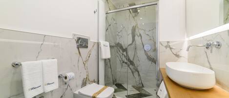 A modern bathroom with a glass shower enclosure, a marble-tiled floor, a white sink, and a bidet.