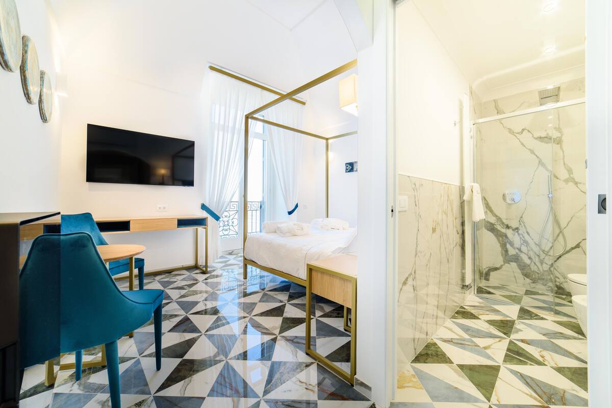 A modern hotel room with a bed, a desk with a chair, a TV, and a shower area.