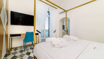 Habitación de hotel con cama, escritorio, silla, televisión y balcón con cortinas.