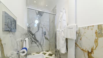 A modern bathroom with a glass shower enclosure, marble walls, and a white sink.