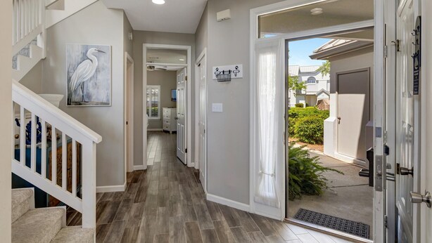 A hallway with a staircase, a painting of a bird, a basket sign, and a door leading outside. - Northshore 3BR Townhouse: Golf Views, Golf Cart, Sandestin Resort Pools (Miramar Beach)