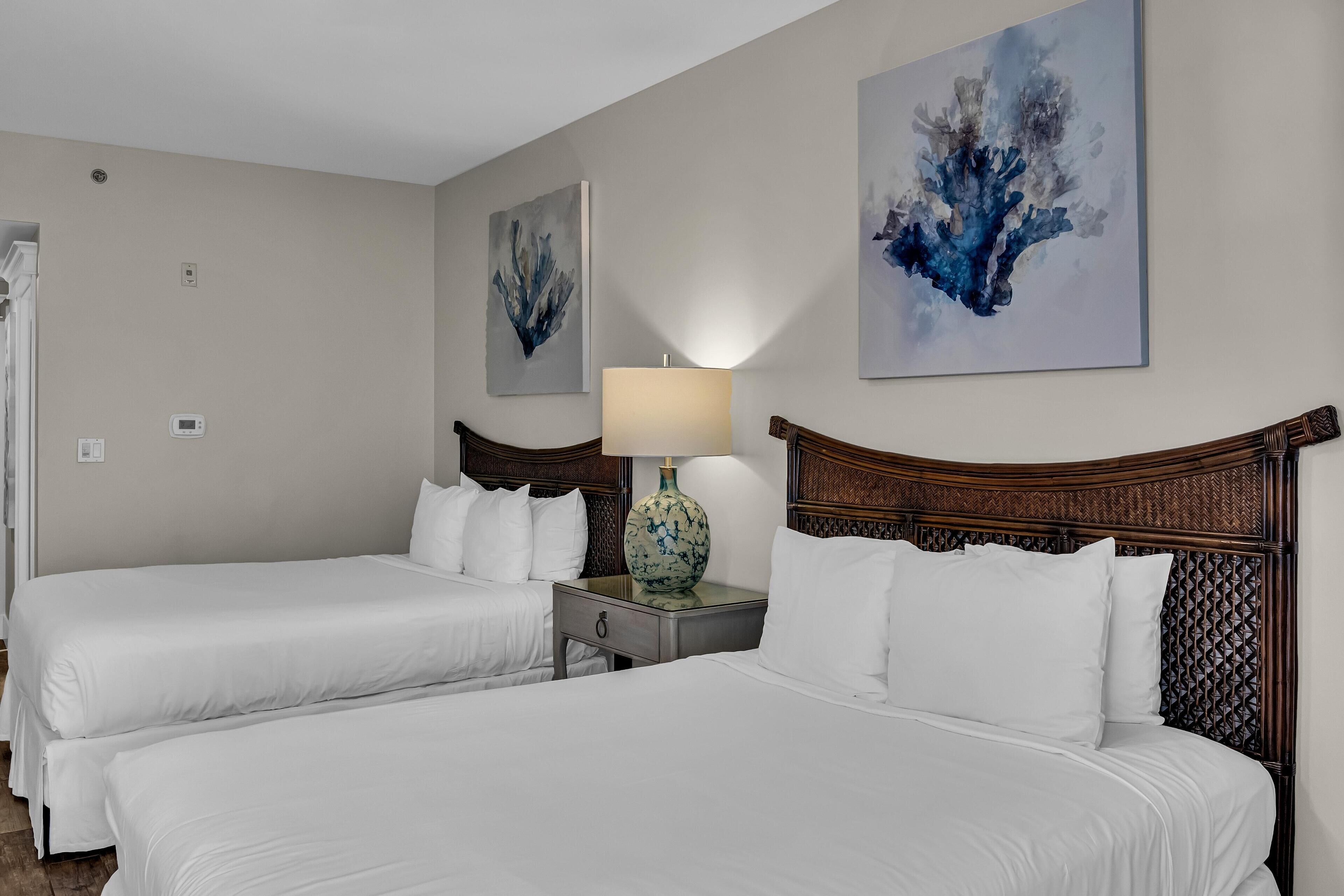 Habitación de hotel con dos camas, una mesita de noche con lámpara y obras de arte en las paredes.