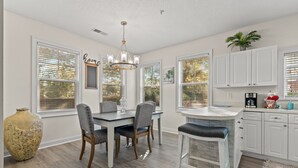 A modern kitchen with white cabinetry, a dining area with a wooden table and chairs, and a large vase.