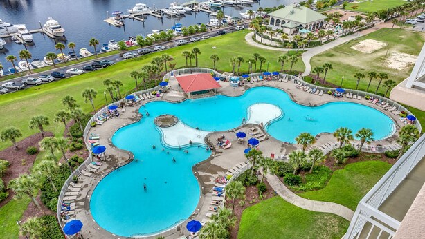 A large, multi-pool resort with a marina, palm trees, and a covered area with umbrellas.