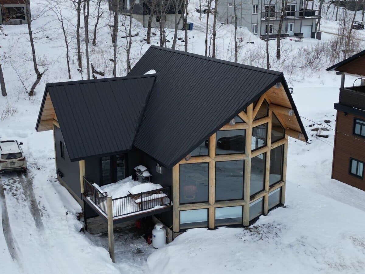 A modern cabin with a large glass window section, a wooden deck, and a metal roof.