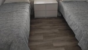 A small, neatly arranged bedroom with two single beds, a central nightstand, and a window with sheer curtains. - Ático con Terraza en los Remedios (Sevilla)