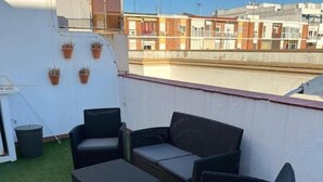 A rooftop terrace with outdoor furniture, potted plants, and a view of buildings in the background. - Ático con Terraza en los Remedios (Sevilla)