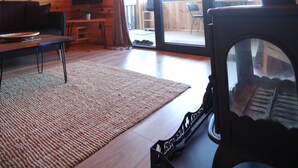 A cozy cabin interior with a wooden ceiling, a fireplace, a sofa, a TV, and a large window. - İnce Bungalov (Sapanca)