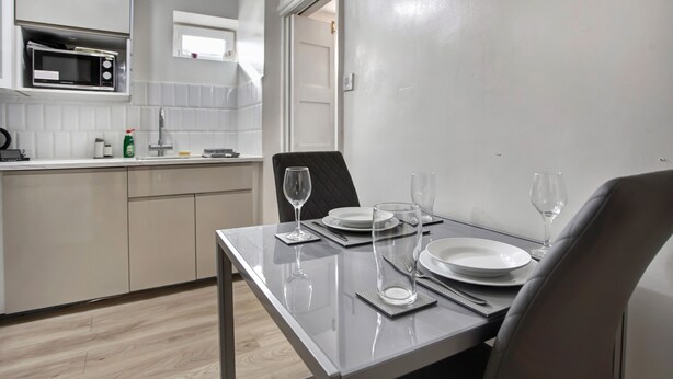 A modern kitchen with a microwave, sink, and cabinets. A dining table with plates, glasses, and cutlery is set. - Cozy 1-bed Apartment Close to Lcy & Excel (London)