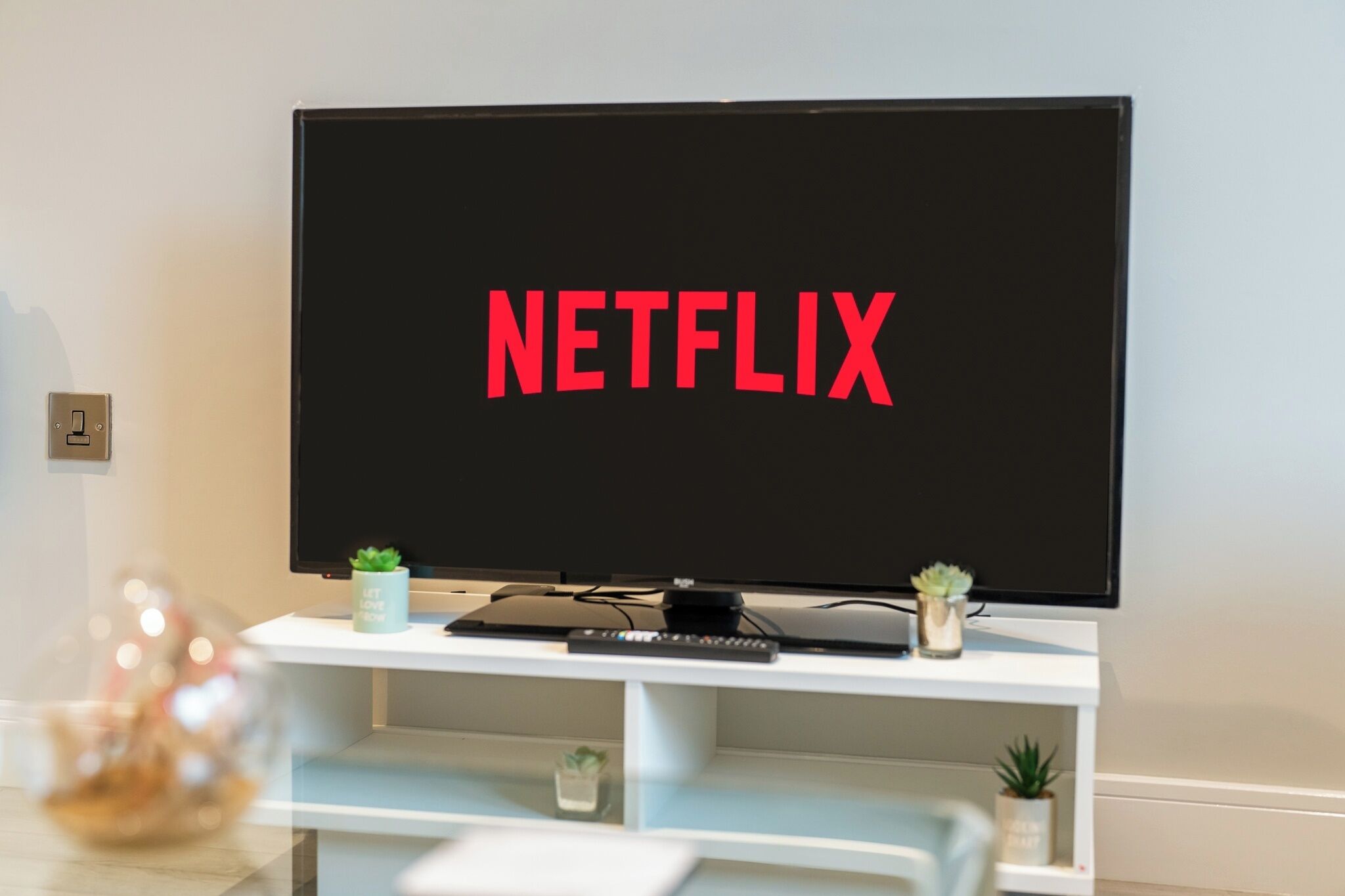 A television with the Netflix logo on the screen, placed on a white entertainment unit with small potted plants.