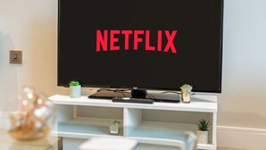 Un televisor con el logo de Netflix en la pantalla, ubicado en un mueble blanco para entretenimiento con pequeñas macetas.
