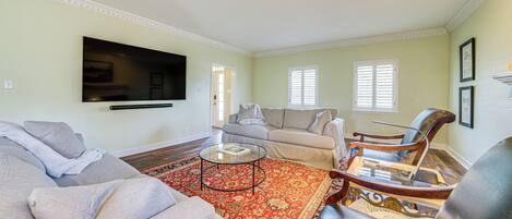 A living room with a sofa, armchairs, a coffee table, and a TV mounted on the wall.