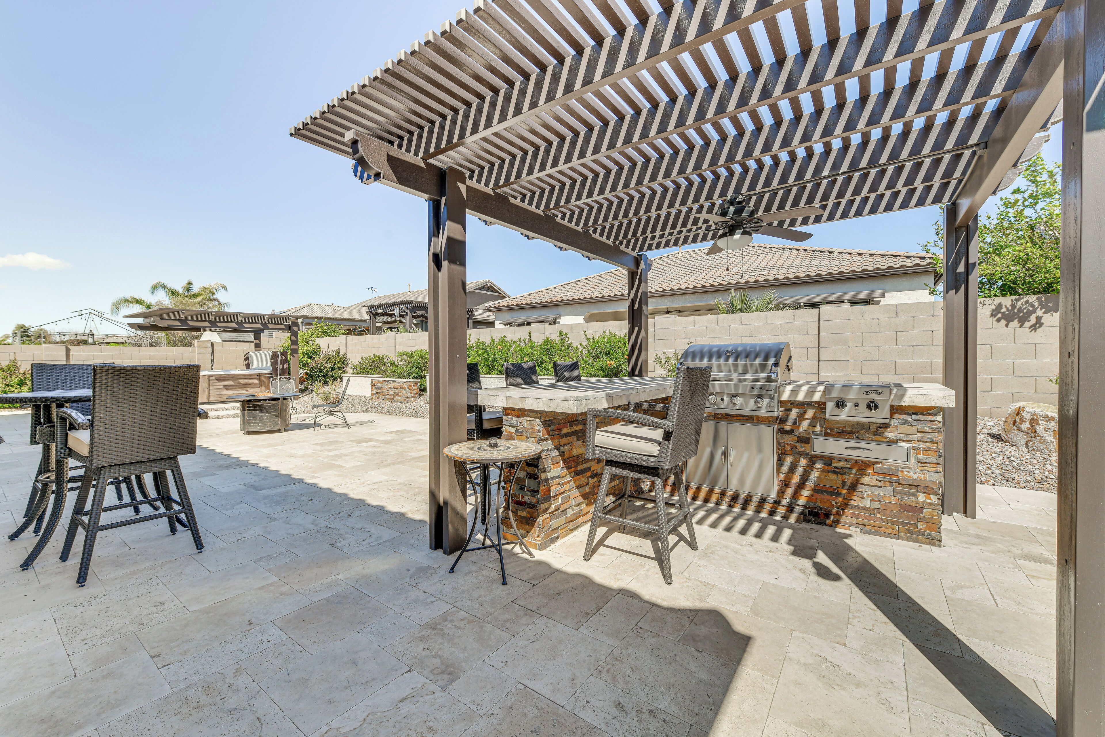 An outdoor patio with a pergola, stone barbecue station, and wicker furniture.