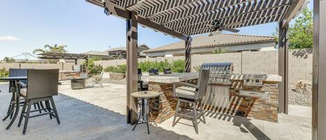 An outdoor patio with a pergola, stone barbecue station, and wicker furniture.