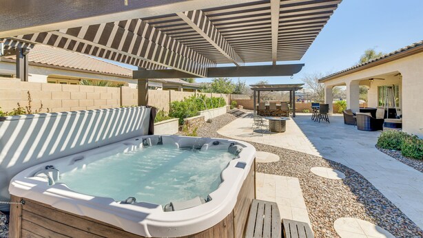 A hot tub under a pergola, surrounded by patio furniture and a stone pathway. - Home w/ Hot Tub & Outdoor Space in Queen Creek! (Queen Creek)