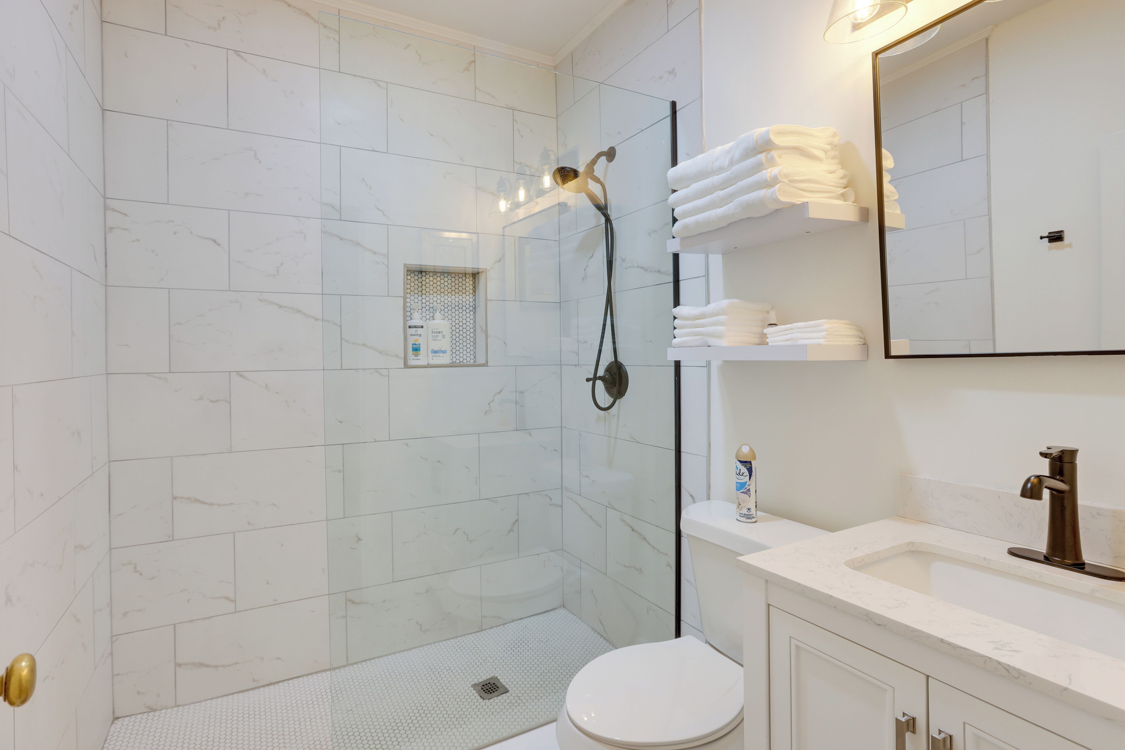 A modern bathroom with a glass-enclosed shower, white marble tiles, a white toilet, and a vanity with a mirror and towel rack.