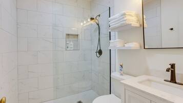 A modern bathroom with a glass-enclosed shower, white marble tiles, a white toilet, and a vanity with a mirror and towel rack.