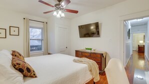 Ein Schlafzimmer mit einem Bett, einem Deckenventilator, einem Schminktisch und einem an der Wand montierten Fernseher.