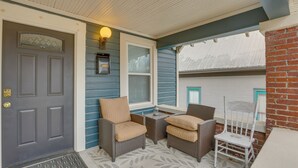 Eine Veranda mit zwei Korbstühlen, einem kleinen Tisch und einer Tür.