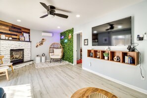 A modern living room with a stone fireplace, wooden shelves, a flat-screen TV, and a ceiling fan. - 5 Mi to Lake Naomi: Home w/ Hot Tub & Fire Pit (Long Pond)