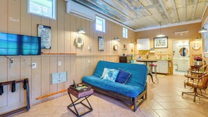 A cozy living area with a blue sofa, wooden walls, and a kitchen in the background. - Inglis Studio Home w/ Covered Patio & Grill! (Inglis)