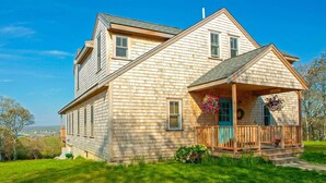 A two-story house with a covered porch and a view of the landscape. - Beautiful Aquinnah Home: Ocean View, Walk to Beach (Aquinnah)