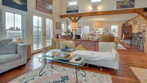 A spacious living room with a large sofa, a coffee table, and a dining area with chairs and a table. - Beautiful Aquinnah Home: Ocean View, Walk to Beach (Aquinnah)