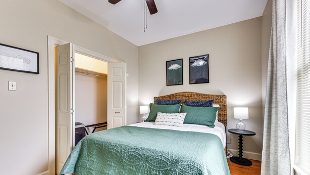 A bedroom with a bed, a bedside table, a lamp, and a door leading to another room.