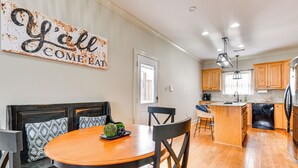 A modern kitchen with wooden cabinets, a central island, and a dining area with a round table and chairs.