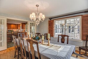 A dining room with a checkered tablecloth, wooden chairs, a chandelier, and a view through a window with shutters. - Expansive Group Getaway < 1 Mi to Dtwn Falmouth! (Falmouth)