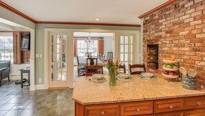 A kitchen with a granite countertop, a brick wall, and a dining area in the background. - Expansive Group Getaway < 1 Mi to Dtwn Falmouth! (Falmouth)