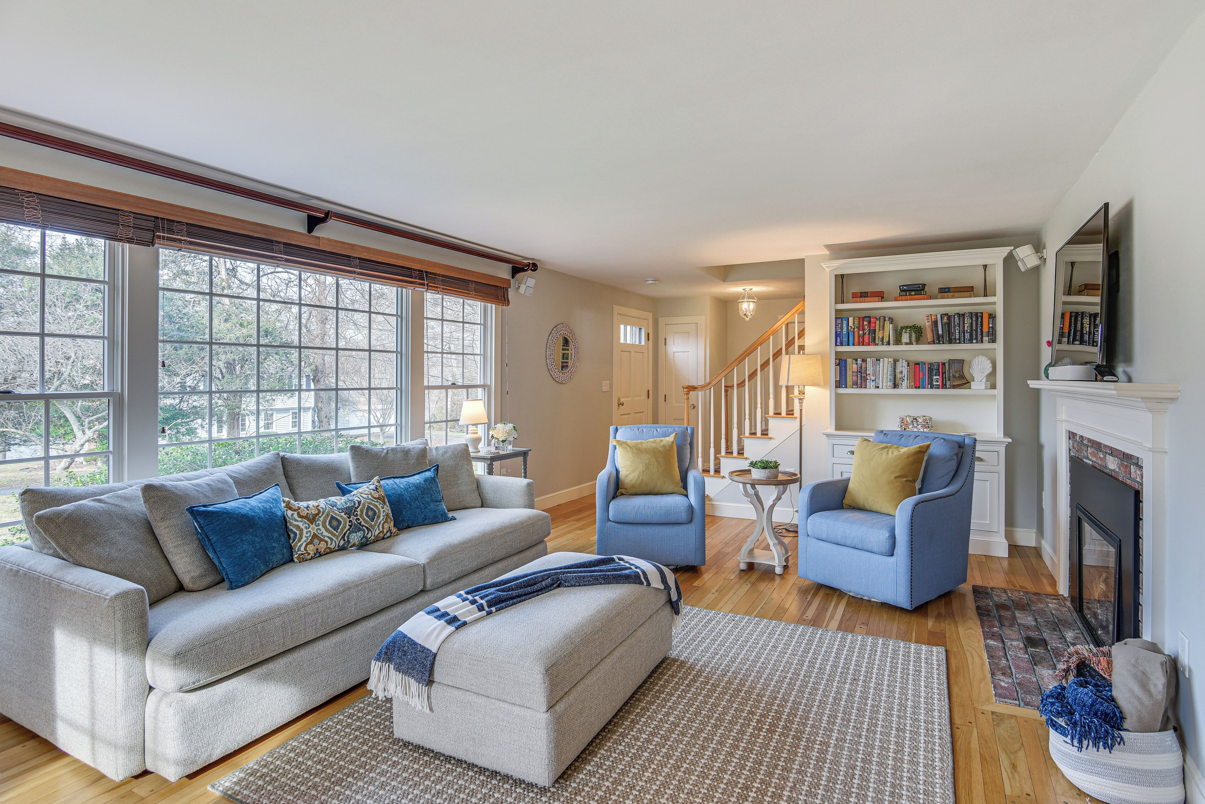 A living room with a sofa, two armchairs, a fireplace, a bookshelf, and a staircase.